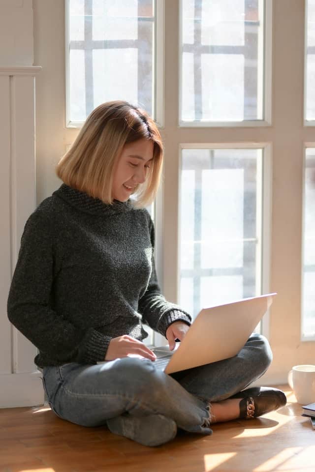 online-billing young woman sitting on floor and typing on laptop